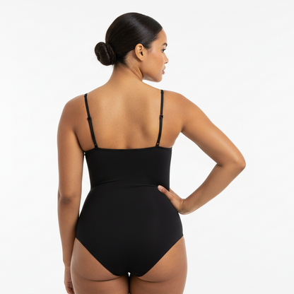 Professional 1:1 studio photo of the same woman. No change in face or body. Natural skin texture. Real pores. Natural imperfections. Thin shoulder straps. Shapewear bodysuit in zwart. Soft white studio lighting. Gentle shadow. Fashion photography look. Back view one hand on hip. Curvy. Warme bruine huid. Low bun. 26 jaar.