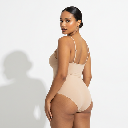 Professional 1:1 studiofoto van dezelfde vrouw. Geen verandering in gezicht of lichaam. Natural skin texture. Real pores. Dunne schouderbandjes. naadloos Shapewear bodysuit in nude. White studio. Zachte schaduw. Luxe fashion vibe. Sexy back POSE. Direct eye contact. Warme bruine huid. Low bun. 26 jaar. Curvy bouw. Real skin.
