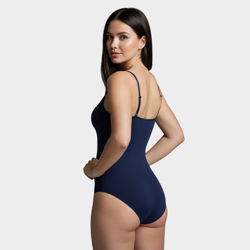 professional 1:1 studiofoto van dezelfde vrouw. geen verandering in gezicht of lichaam. real skin texture. real pores. natural imperfections. dunne schouderbandjes. shapewear bodysuit in kleur #0c1a3c. smooth matte 4D stretch. soft grey studio. pose back view met één hand in de zij en hoofd licht gedraaid naar camera. powerful confident. Lichte huid, slim thick body, straight donker hair mid length, 25 jaar, zachte confident blik.