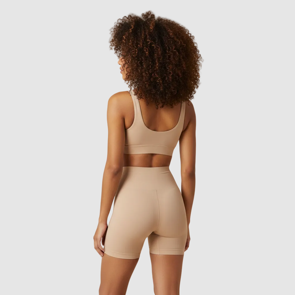 Studio photo, same female model, 28 years old, vol tan skin, tight natural curls. Wearing nude high-waisted sculpt shorts and matching bra. Back view. High-waisted sculpt shorts ending mid-thigh, approx 8–10 cm above the knee, straight hem. Focus on smooth glute shaping. Clean light beige background. Ultra realistic. 800x800.
